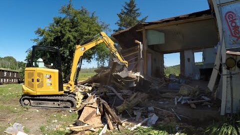 A cat mini excavator demolishing a small structure.